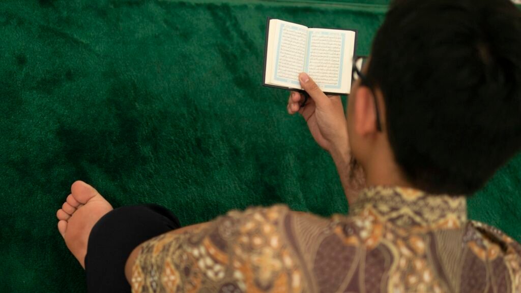 Seseorang membaca mushaf kecil di atas karpet hijau