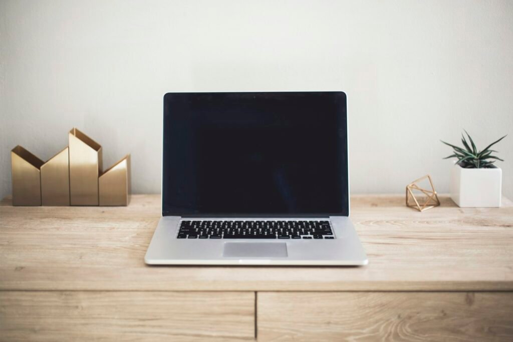 Laptop di atas meja kayu dengan tanaman kecil